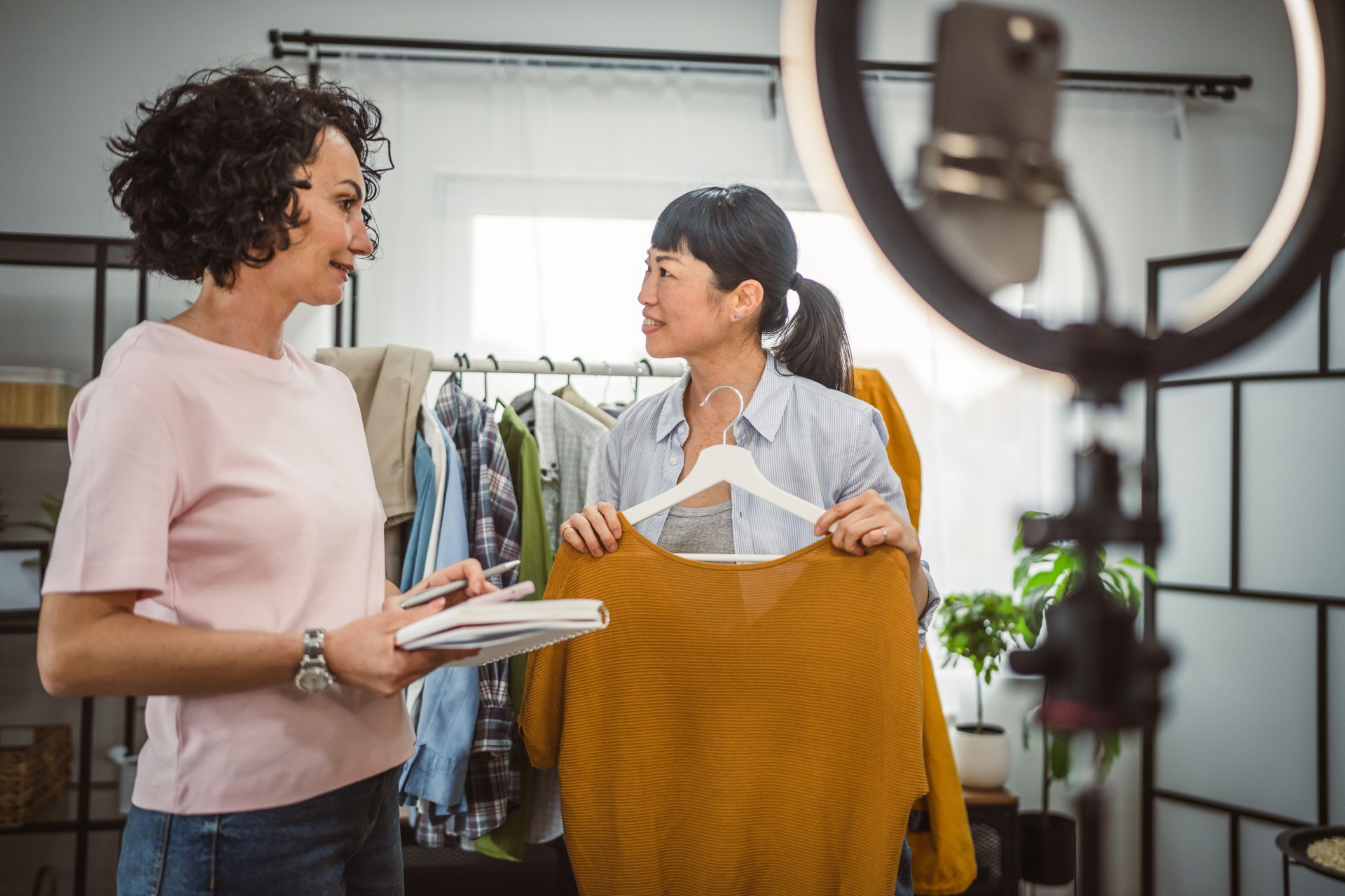 Two diversity woman sell clothes live stream on mobile phone at home